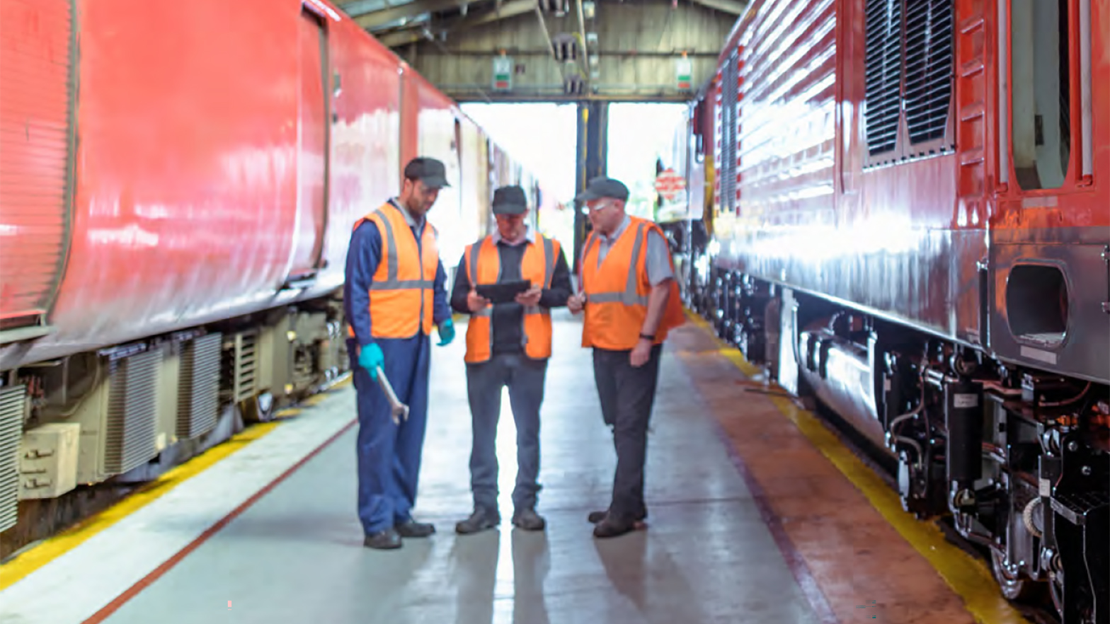 三个工人穿着橙色背心和安全设备站在两个停列车